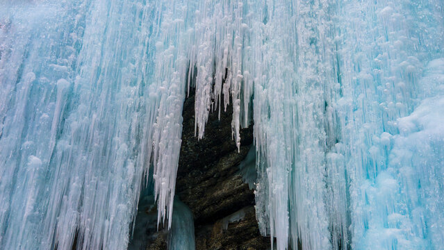 Aerial view of frozen waterfall with intricate icicles hanging over dark rock face in Khunjerab National Park, Gilgit-Baltistan, Pakistan.