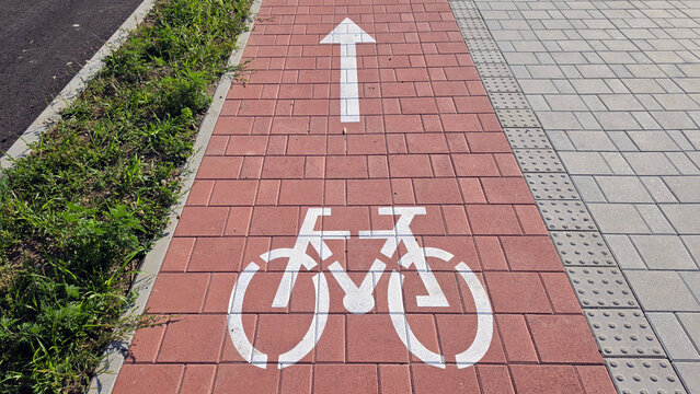 Painted white bicycle lane symbol and forward arrow on a red brick paving stone path