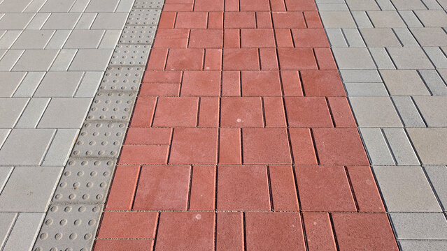 Red interlocking brick path flanked by grey concrete pavers and tactile paving blocks