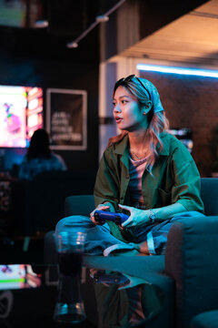 Woman playing video game with controller in neon-lit setting