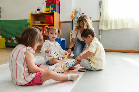 Teacher helping toddlers drawing and learning in classroom