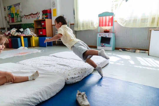 Preschool boy jumping on soft mats in classroom