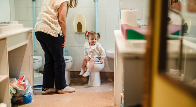 Little girl learning potty training with adult supervision