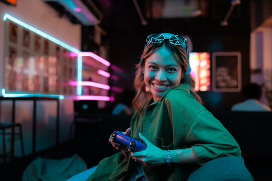Woman smiling while holding game controller in neon-lit setting