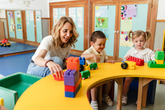 Teacher helping toddlers playing colorful building blocks classroom