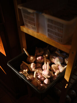 Garlic stored in a basket on a wooden shelf in a kitchen