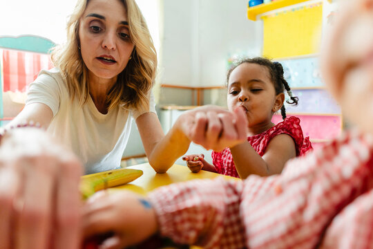Teacher helping diverse student with snack in kindergarten