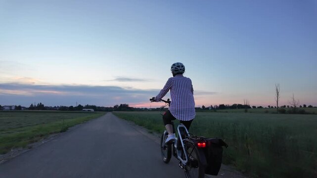 Middle aged woman riding electric bicycle on paved path through green fields