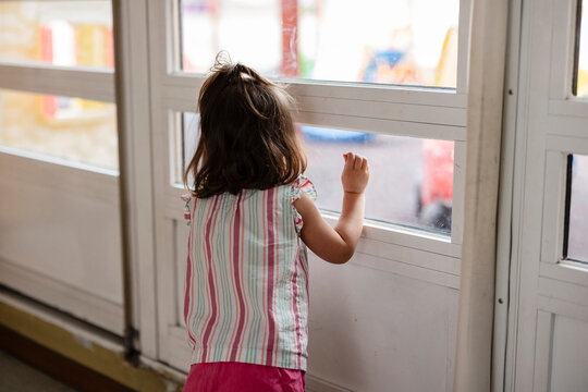 Little girl watching outside through window glass