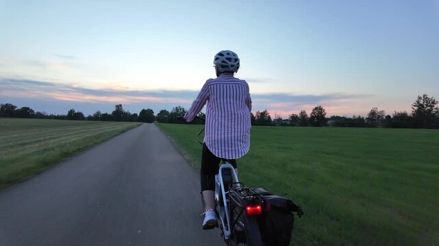 Middle aged woman riding electric bicycle on paved path through green fields