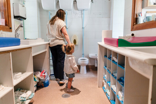 Caregiver assisting young child using toilet in nursery bathroom