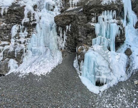 Aerial view of a frozen waterfall cascading down a rugged rocky cliff face with a gravel slope at the base in Khunjerab National Park, Gilgit, Pakistan.