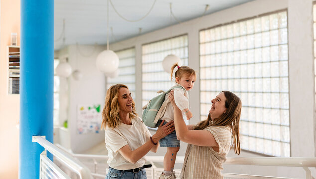 Two mothers playing with daughter wearing backpack