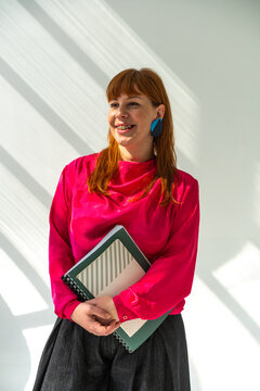 Smiling Redhead Woman Holding Notebook in Bright Pink Blouse 