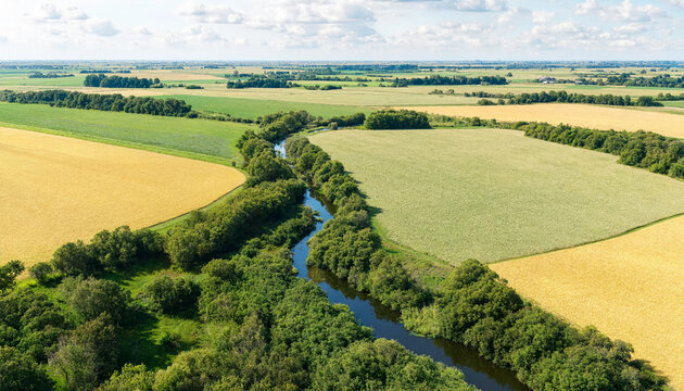 Aerial view of a narrow river flowing through agricultural fields and lush green meadows on a sunny day in the countryside with agriculture farmland landscape countryside waterway peaceful