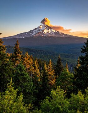 Majestic snow-capped volcano erupts with a plume of smoke against a clear blue sky at sunrise.