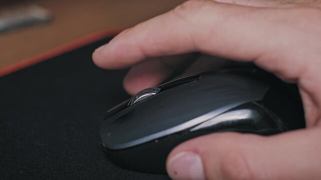 Side angle view of a male hand navigating with a wireless black mouse on a dark desk mat. The ergonomic usage suggests professional corporate workflow or a dedicated gaming session.