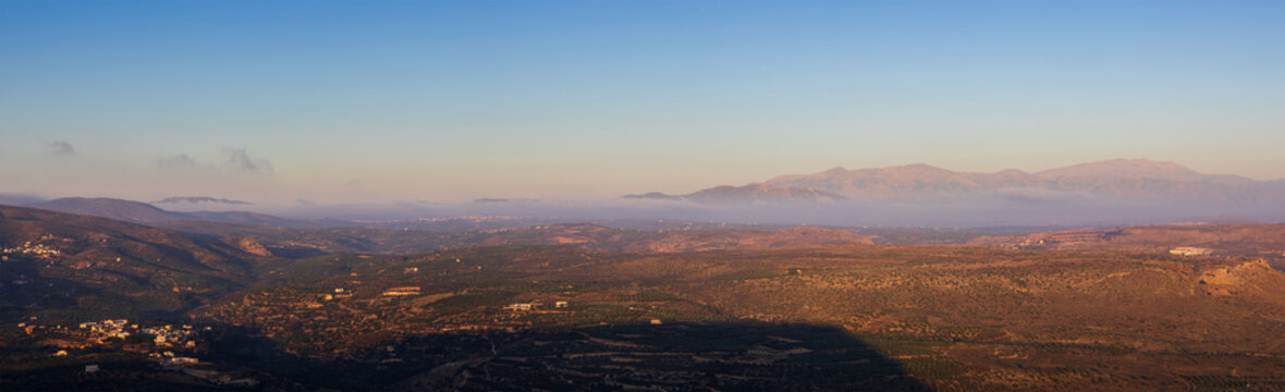 Panoramic morning view of Gouves village in Crete, Greece, taken from Mount Edheri with layer of low fog and misty horizon during sunrise