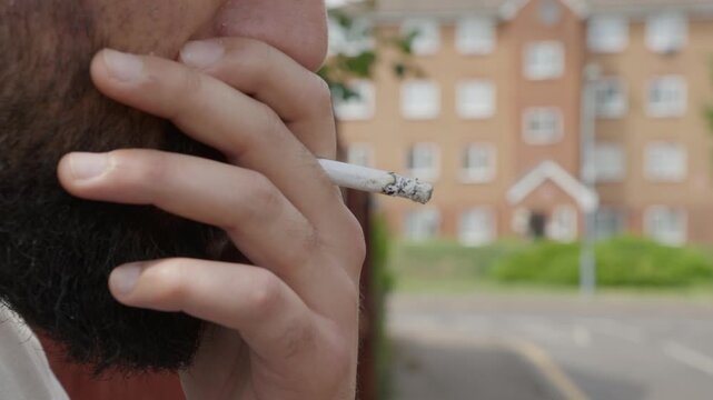 Close-up of a bearded man smoking a cigarette outdoors, bad habit and addiction concept.