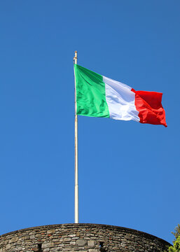 Italian national flag waving in the wind on a flagpole above a stone castle tower in Bergamo Italy against a clear blue sky
