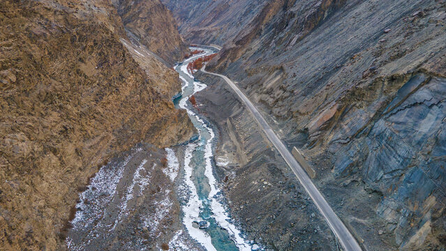 Aerial view of the winding river and Karakoram Highway cutting through the rugged Khunjerab pass with rocky slopes and patches of snow in Hunza Nagar, Gilgit, Pakistan.