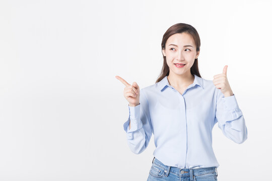 Smiling young woman pointing sideways and showing thumbs up on white background