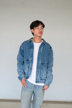 Young Asian non-binary man standing in denim jacket looking away
