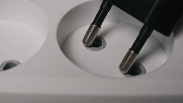Macro top-down view of a hand unplugging a black power cord from a white electrical outlet. The user disconnects a device from the energy supply to save electricity and money.