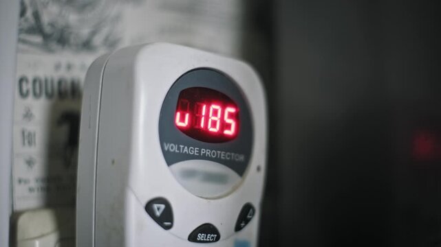 Close-up of a voltage protector digital display showing a low unstable current. The safety device activates to cut power and protect appliances from grid failure.