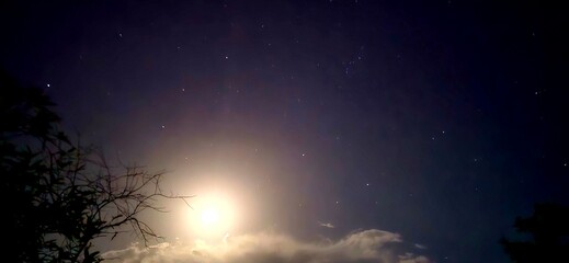 Fototapeta premium Starry night sky with bright full moon, glowing celestial landscape over dark clouds, atmospheric astronomical background with twinkling stars