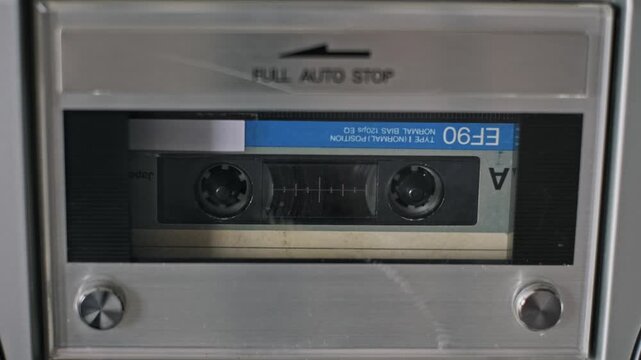 Close-up shot of a hand opening a silver cassette deck to swap audio tapes. The mechanical door on the vintage player closes and reopens to change the media.