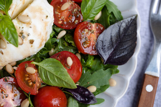 Close up a mix of greens, cherry tomatoes, fresh basil, and cheese. Pine nuts scatter on top. Healthy eating concepts, and Italian cuisine. top view