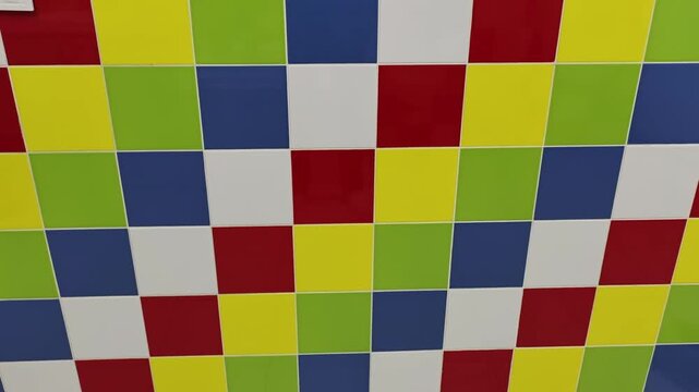 Camera pans up a wall featuring a checkerboard pattern of bright multicolored ceramic square tiles. Concept of interior design renovation, geometric backdrops, and modern playful decoration.