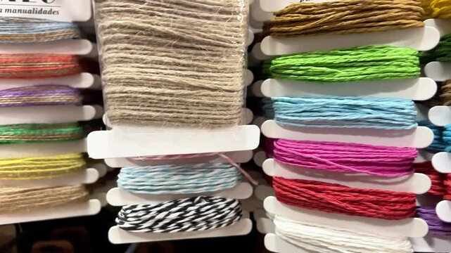 Different colors of threads are arranged neatly on spools in a craft store. Customers look at the threads to choose their favorites for various projects.