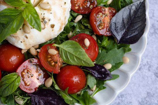 Close up a mix of greens, cherry tomatoes, fresh basil, and cheese. Pine nuts scatter on top. Healthy eating concepts, and Italian cuisine. top view