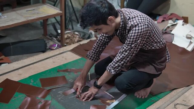 Midframe shows a skilled artisan kneeling on a workshop floor, carefully cutting brown leather scraps on a green cutting mat and assembling pieces, capturing