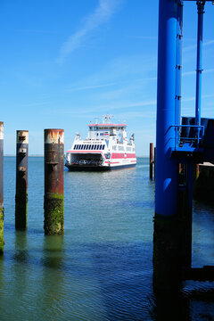 A vertical high-angle shot of a passenger and car ferry arriving at the harbor of Wyk auf F&ouml;hr, Germany, maneuvering between metal poles and the ferry terminal bridge.