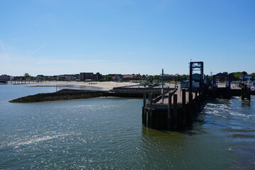 Fototapeta premium A scenic view from a departing passenger ferry looking back at the blue harbor terminal, the calm sea water and the coastline of Wyk auf Föhr, Germany.