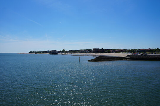 A scenic wide panoramic view across the blue water of the North Sea towards the silhouette of Wyk auf F&ouml;hr on the horizon under a clear blue sky, Germany.