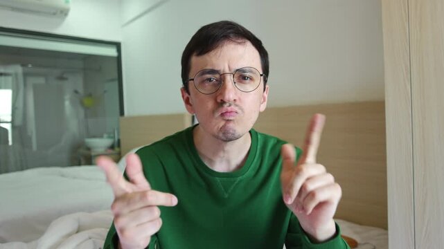 Funny and eccentric man with glasses executing serious and slightly crazy no-no-no finger wagging dance. Stern-faced goofy guy making exaggerated gestures directly to the camera during a video call