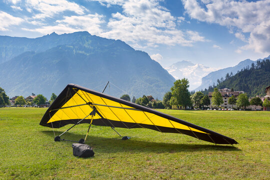 Hang glider on a grassy field with alpine mountains and glacier peaks near Interlaken, Bernese Oberland, Switzerland.