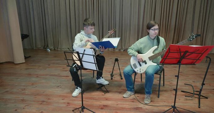 Boy and Girl Practice Playing Music on Stage. Kids Play Guitar and Bass Guitar. 4K 10-bit
