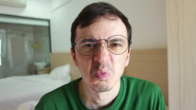 Man with glasses showing a strong negative emotion, wrinkling his nose and pursing his lips in revulsion as he looks directly at the camera, portraying a feeling of utter disgust