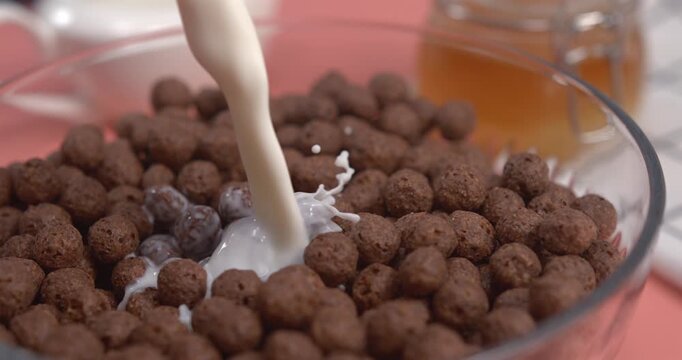 Fresh milk pouring into chocolate cereal balls bowl creating dynamic splash in ultra slow motion