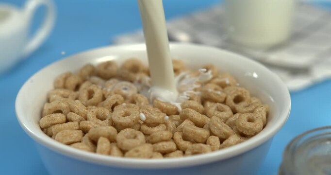 Milk pouring into wheat cereal rings in bowl with splash in super slow motion