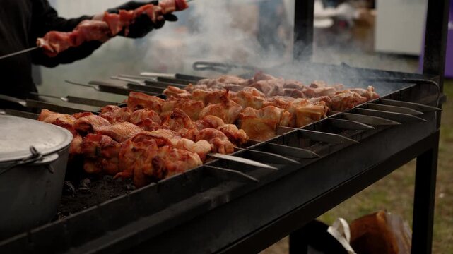 Cook turns marinated meat skewers on outdoor metal grill. Preparation of barbecue shish kebab over hot charcoal. Culinary process of grilling food in backyard.