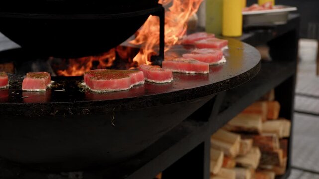 Raw fish steak cooking on a rustic metal fire pit. Salmon fillet grilling over open flames in outdoor kitchen. Culinary process of preparation fresh seafood.