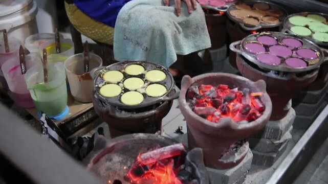 Traditional Indonesian mini pancakes cooking in round molds over charcoal stoves, authentic street food preparation with colorful batter and rustic kitchen atmosphere.