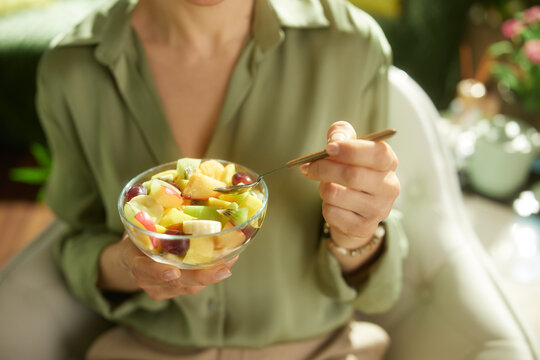 A close-up view of a person in a green blouse holding a clear glass bowl of mixed fruit, symbolizing healthy food choices and nutritional wellness.
