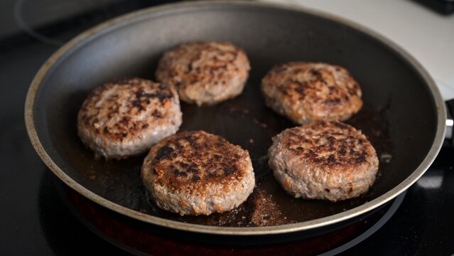 Beef and turkey patties frying in black pan on electric stovetop. Food photography. Homemade meat cutlets and cooking concept.